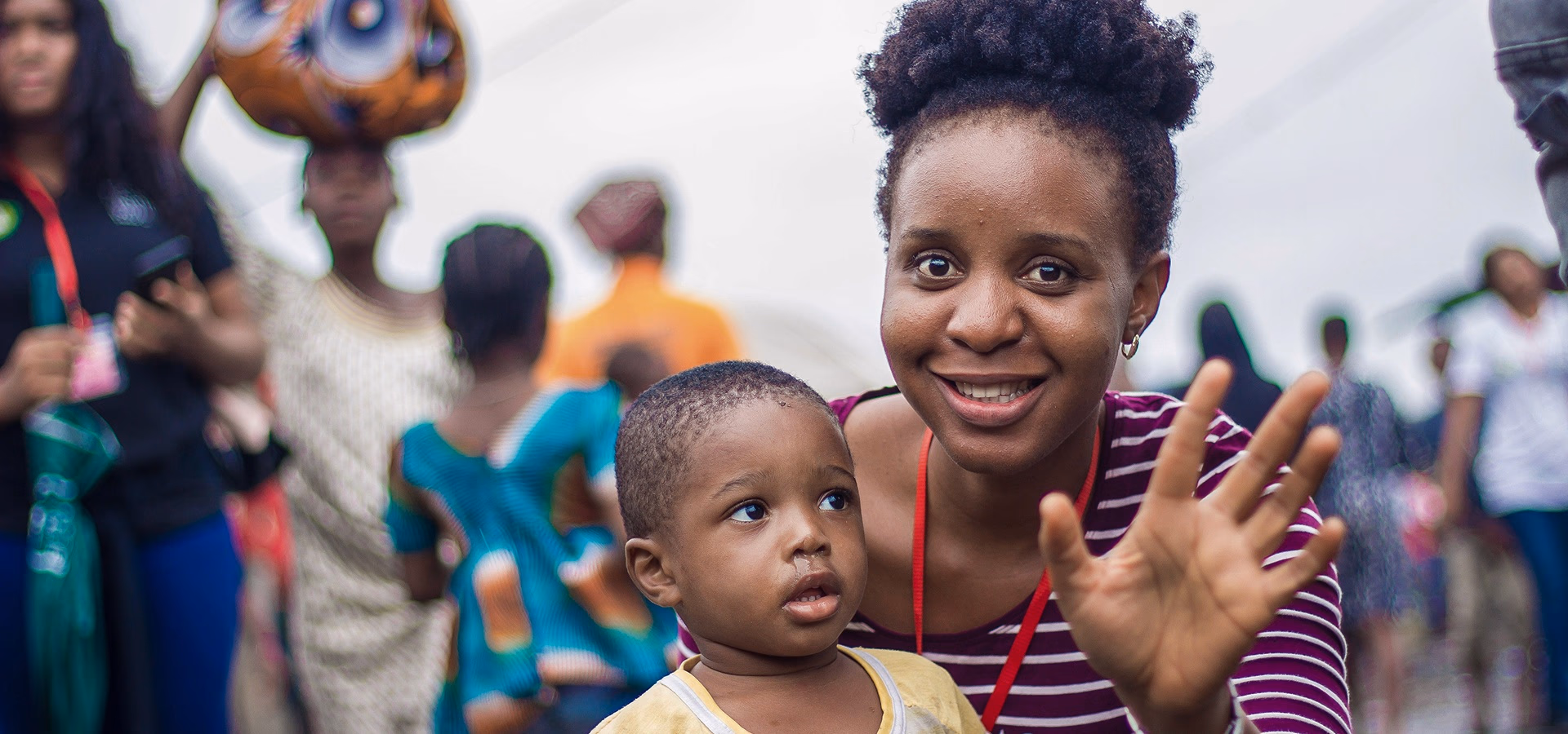A young woman waving while holding a child